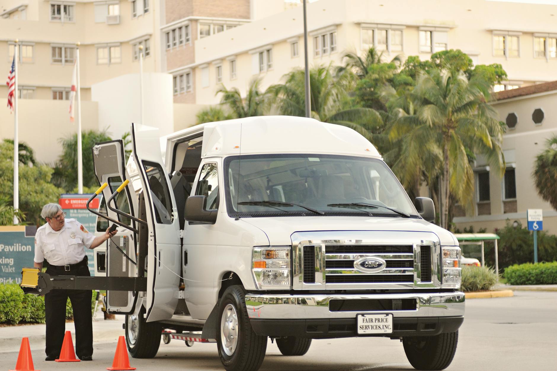 Accessible passenger van with a wheelchair lift and an attendant standing outside a medical facility.