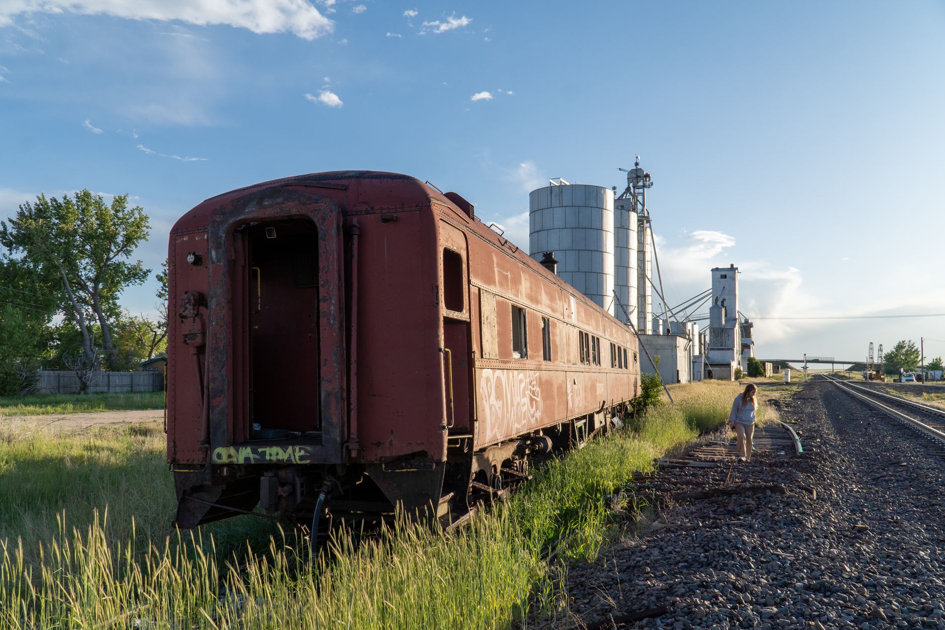 A rusty rail car sits beside tracks and grain silos in Strasburg, Colorado.