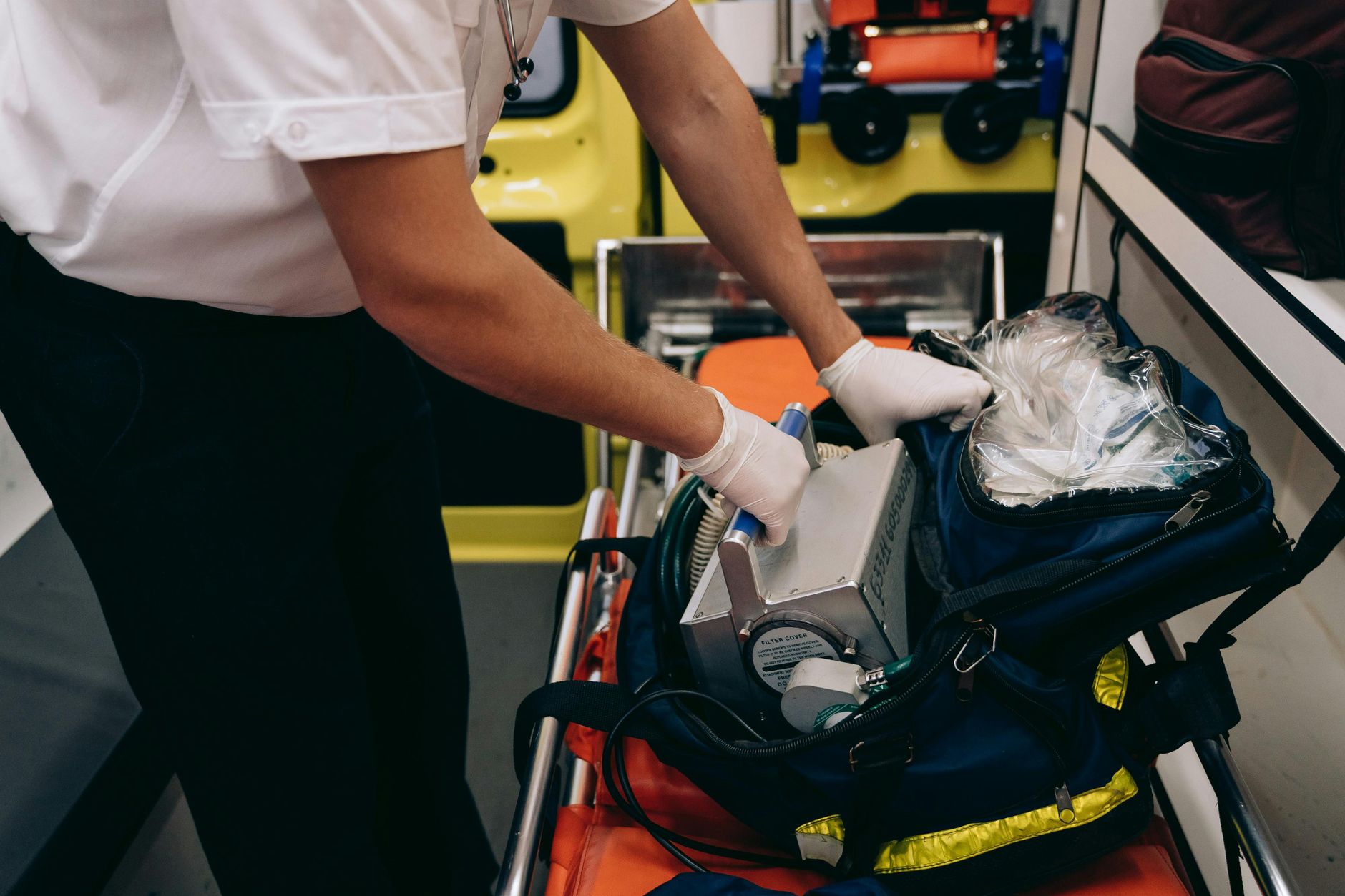 A paramedic wearing gloves organizes equipment inside an ambulance.