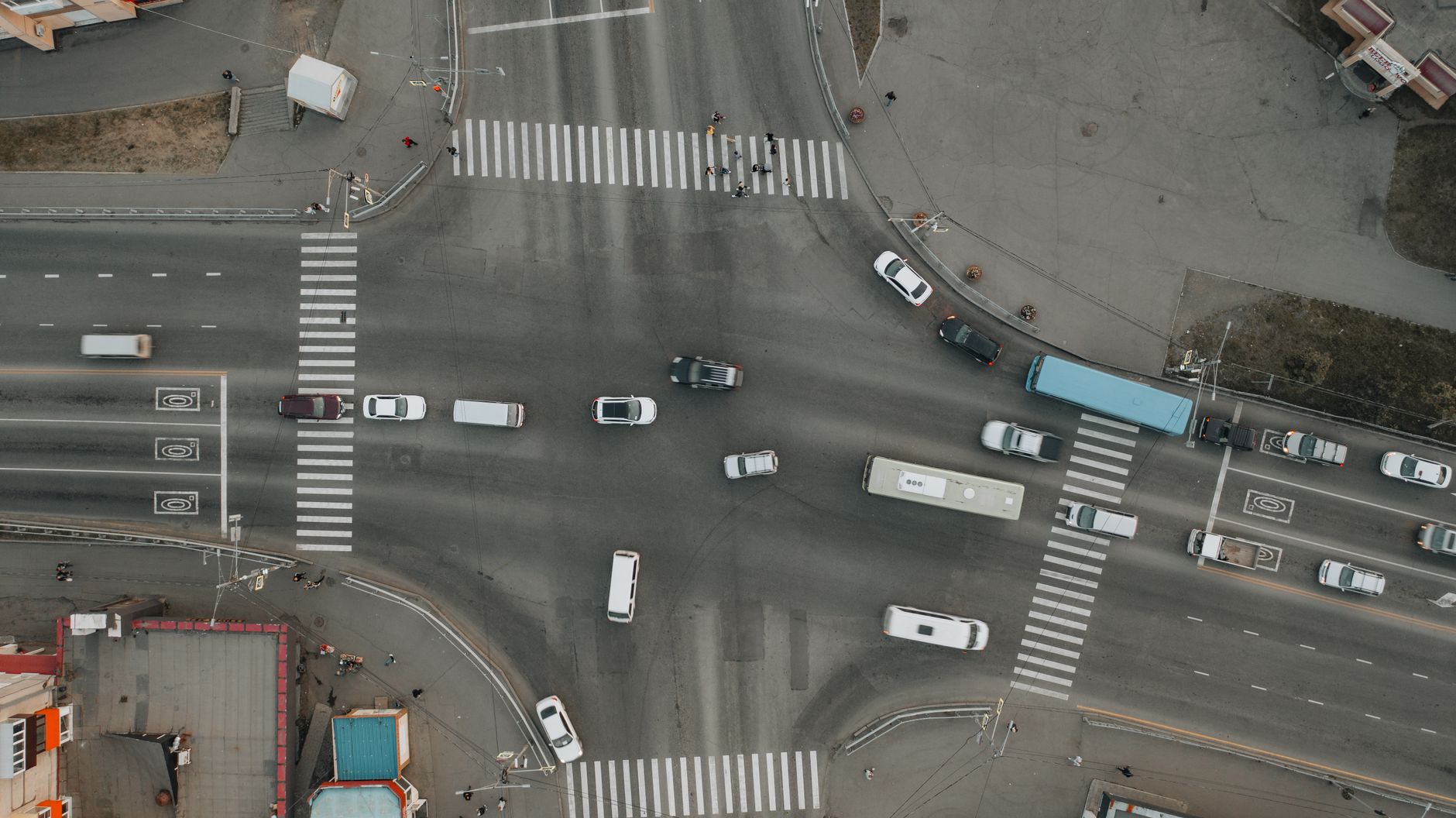 Aerial view of a city intersection with crosswalks and moving vehicles.