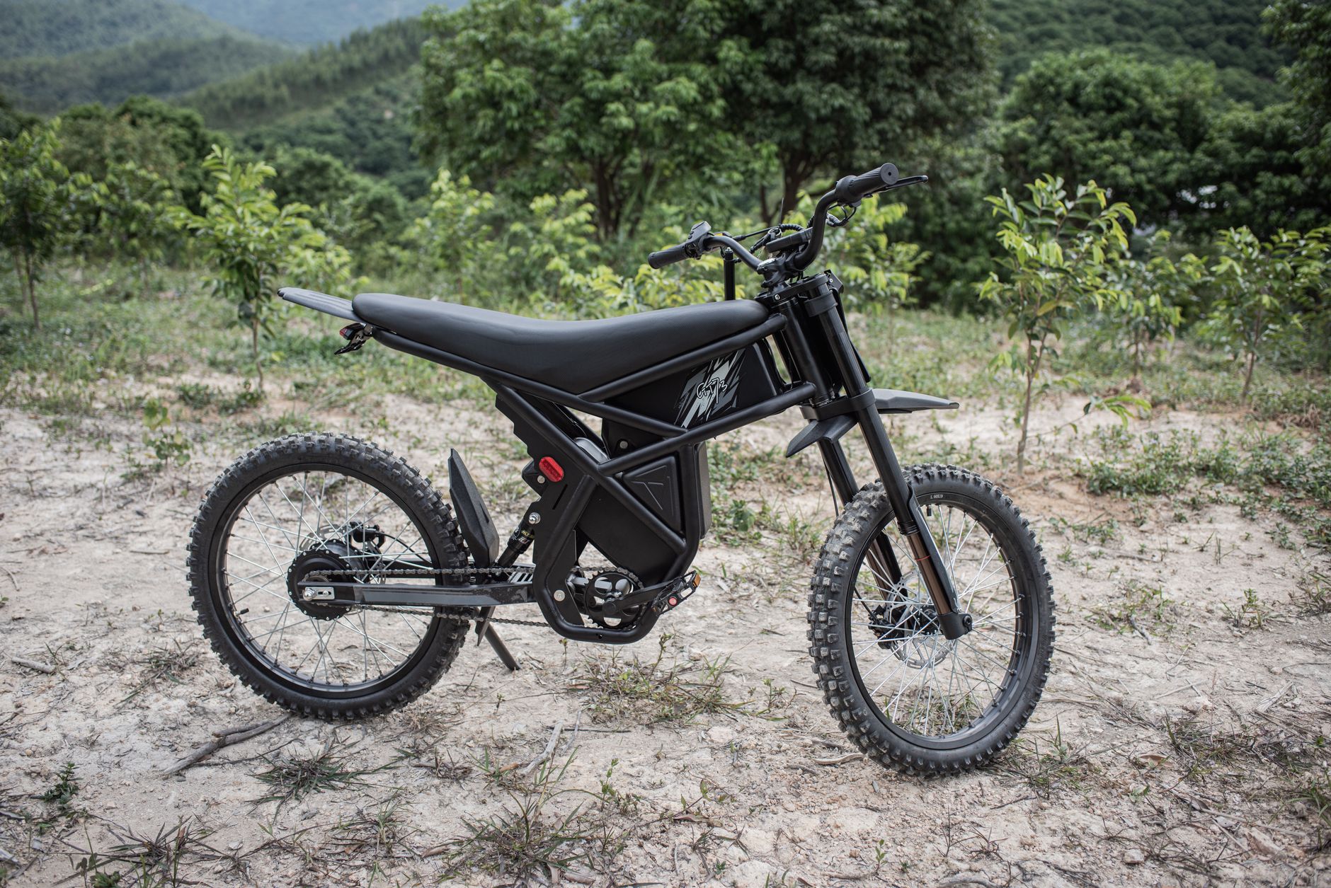 An electric dirt bike is parked in a wooded outdoor area.