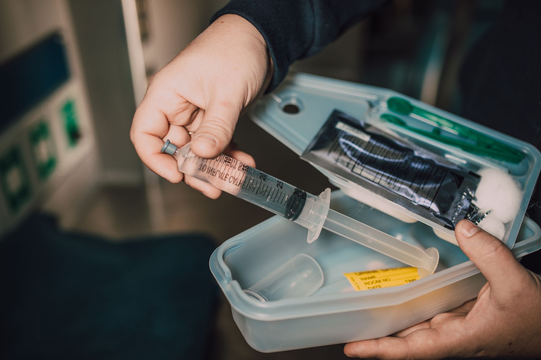 A hand holds a syringe among medical supplies in a kit.
