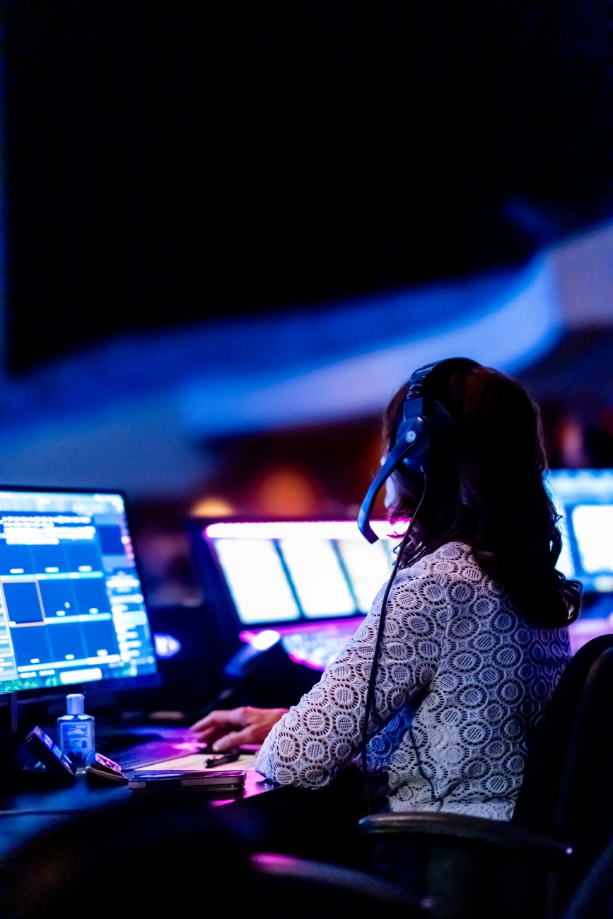 A dispatcher wearing a headset works at a desk with multiple computer screens.