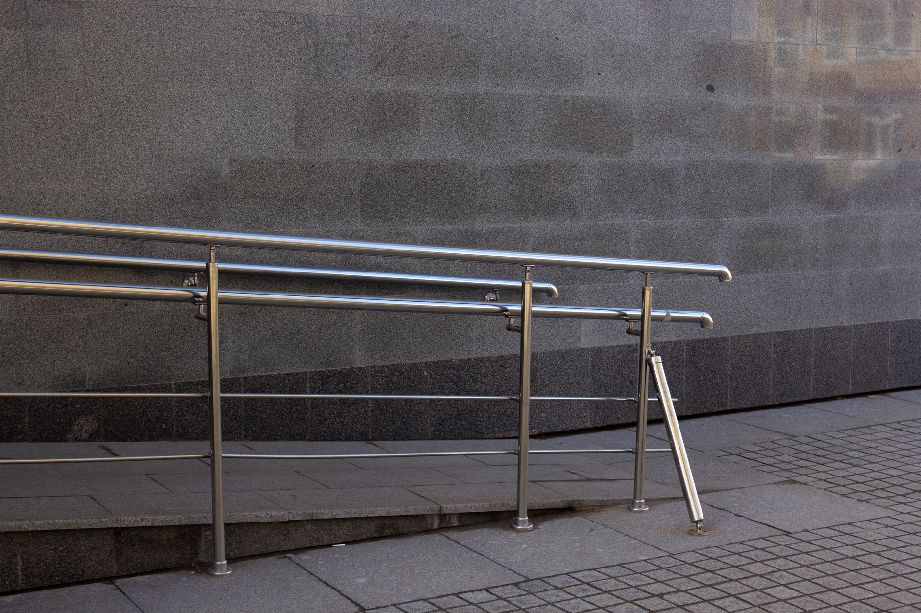 A concrete ramp with a metal handrail beside a sidewalk.
