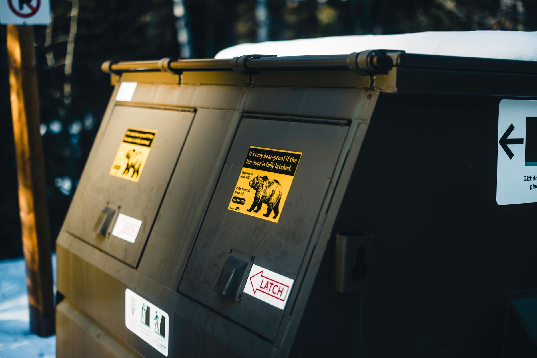 A bear-resistant dumpster with wildlife-safety warning signs.