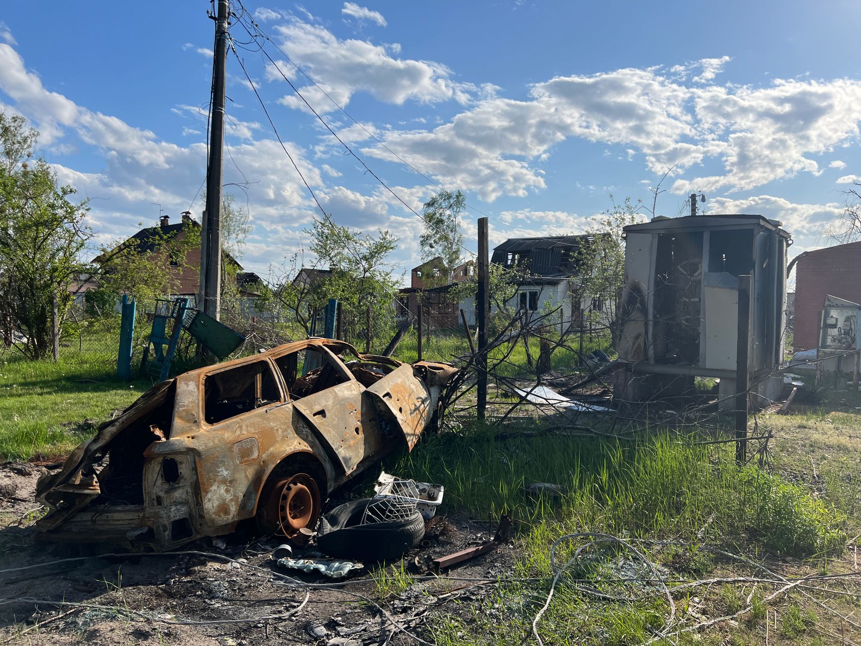An old car and scattered debris sit in an overgrown yard.