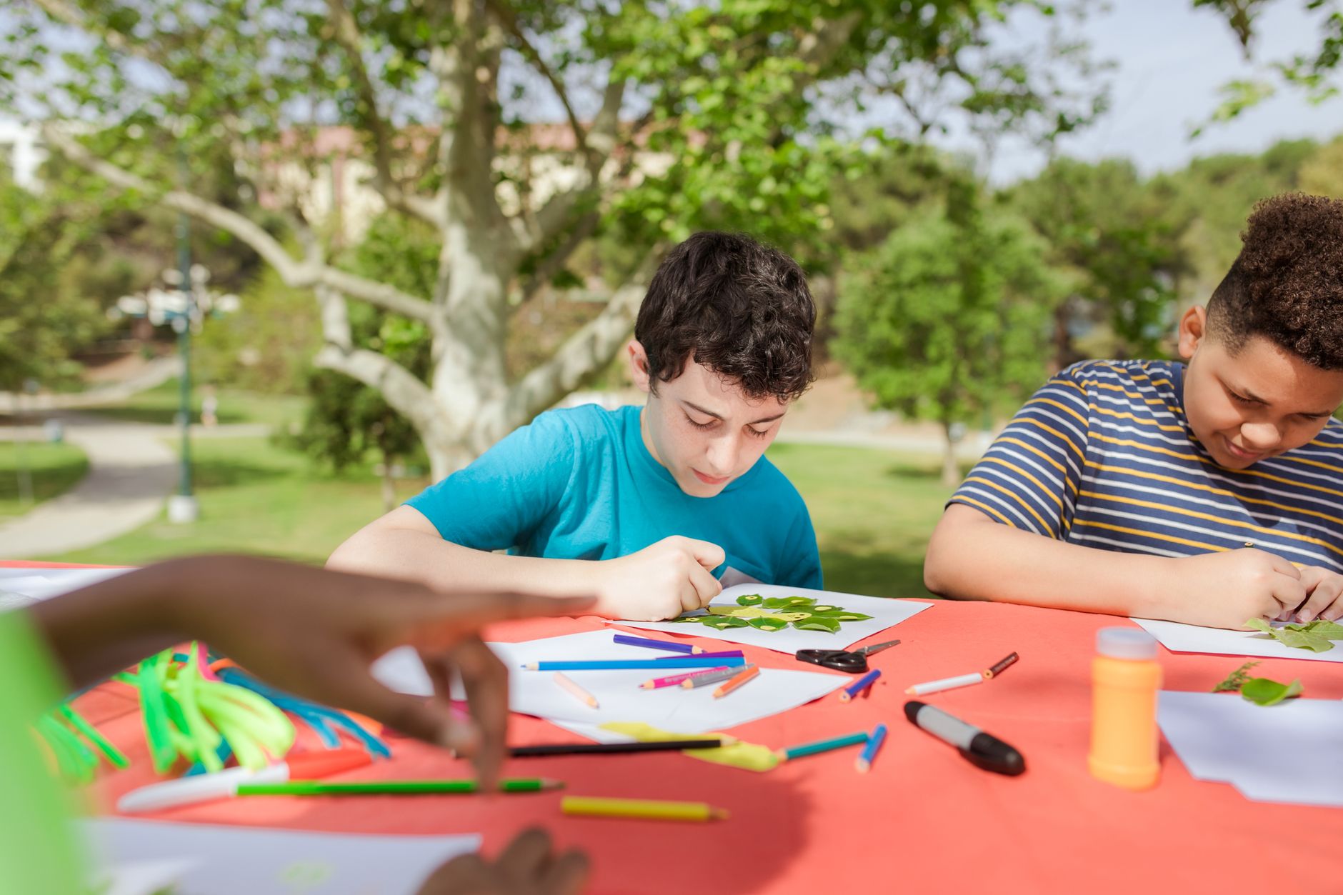Children make crafts together at an outdoor table.