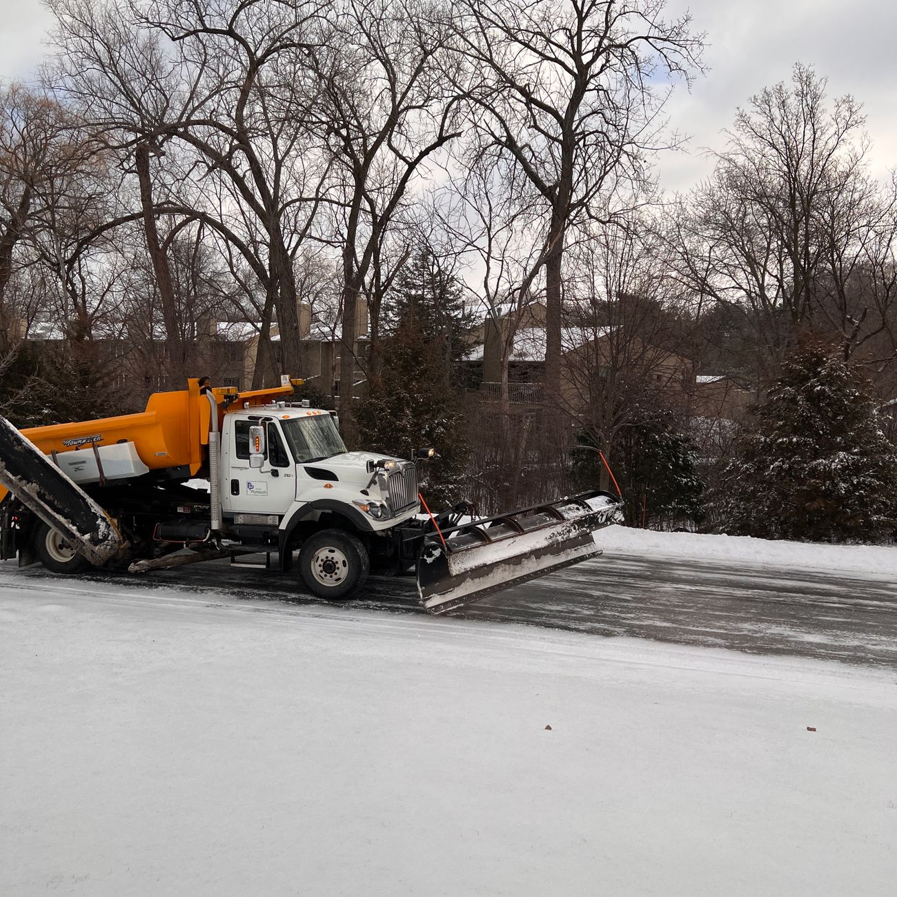 A snowplow clears a snow-covered residential street.